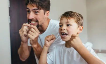 Vater und Sohn, lächeln und putzen sich gemeinsam die Zähne vor einem Badezimmerspiegel.